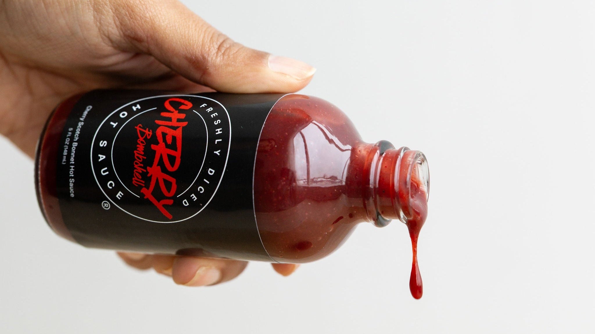Hand holding a bottle of cherry sauce with a white background